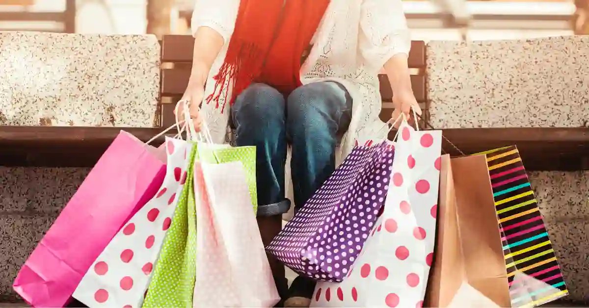 how-to-build-emotional-resilience-around-money A person sitting on a bench holding several colorful shopping bags, symbolizing the journey towards building emotional resilience around money and spending habits