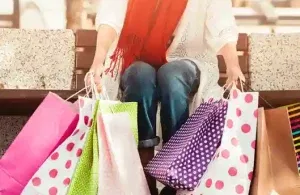 A person sitting on a bench with several colorful shopping bags, symbolizing emotional spending and impulse buying.