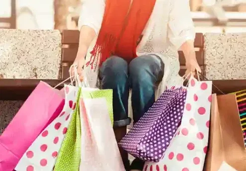 A person sitting on a bench with several colorful shopping bags, symbolizing emotional spending and impulse buying.