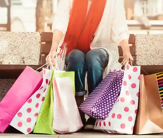 A person sitting on a bench with several colorful shopping bags, symbolizing emotional spending and impulse buying.