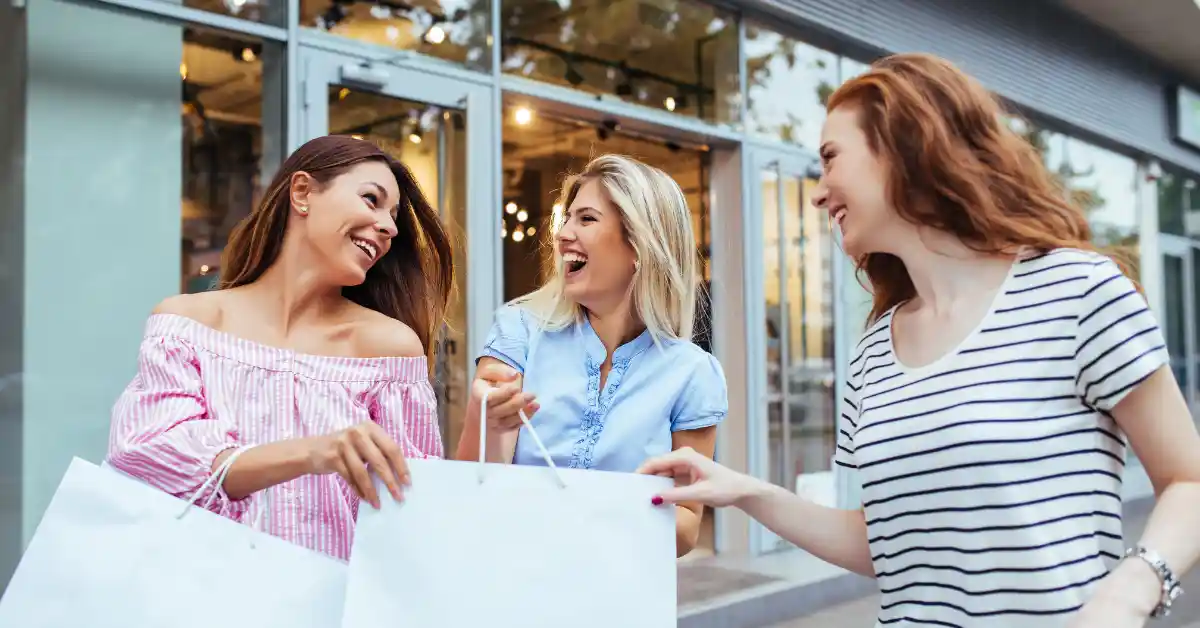 mindful-money-approach Three women chatting and smiling after shopping, sharing a positive moment outside store windows.