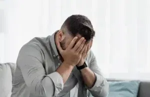 Sitting on a couch with their face in their hands, representing the emotional impact of shame on mental health