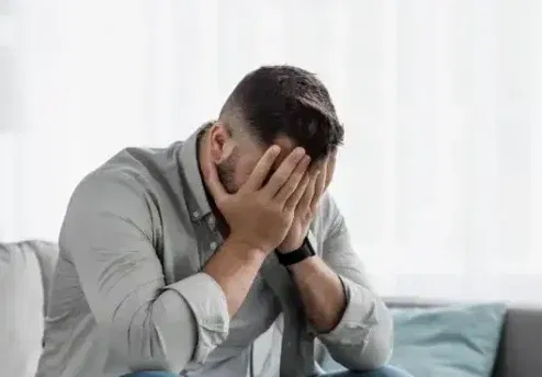 Sitting on a couch with their face in their hands, representing the emotional impact of shame on mental health