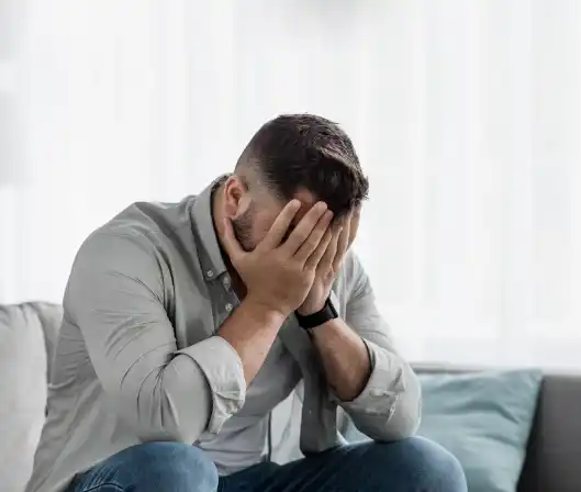 Sitting on a couch with their face in their hands, representing the emotional impact of shame on mental health