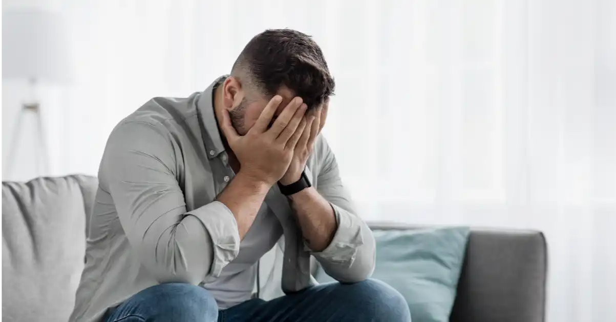 shame-impact-mental-health-blog A person sitting on a couch with their face in their hands, representing the emotional impact of shame on mental health